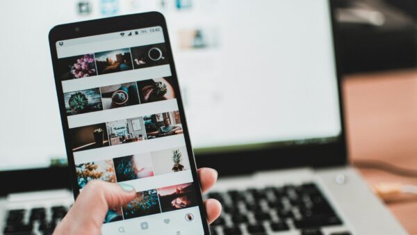 A person uses a smartphone to browse social media in front of a laptop, emphasizing modern technology and lifestyle.